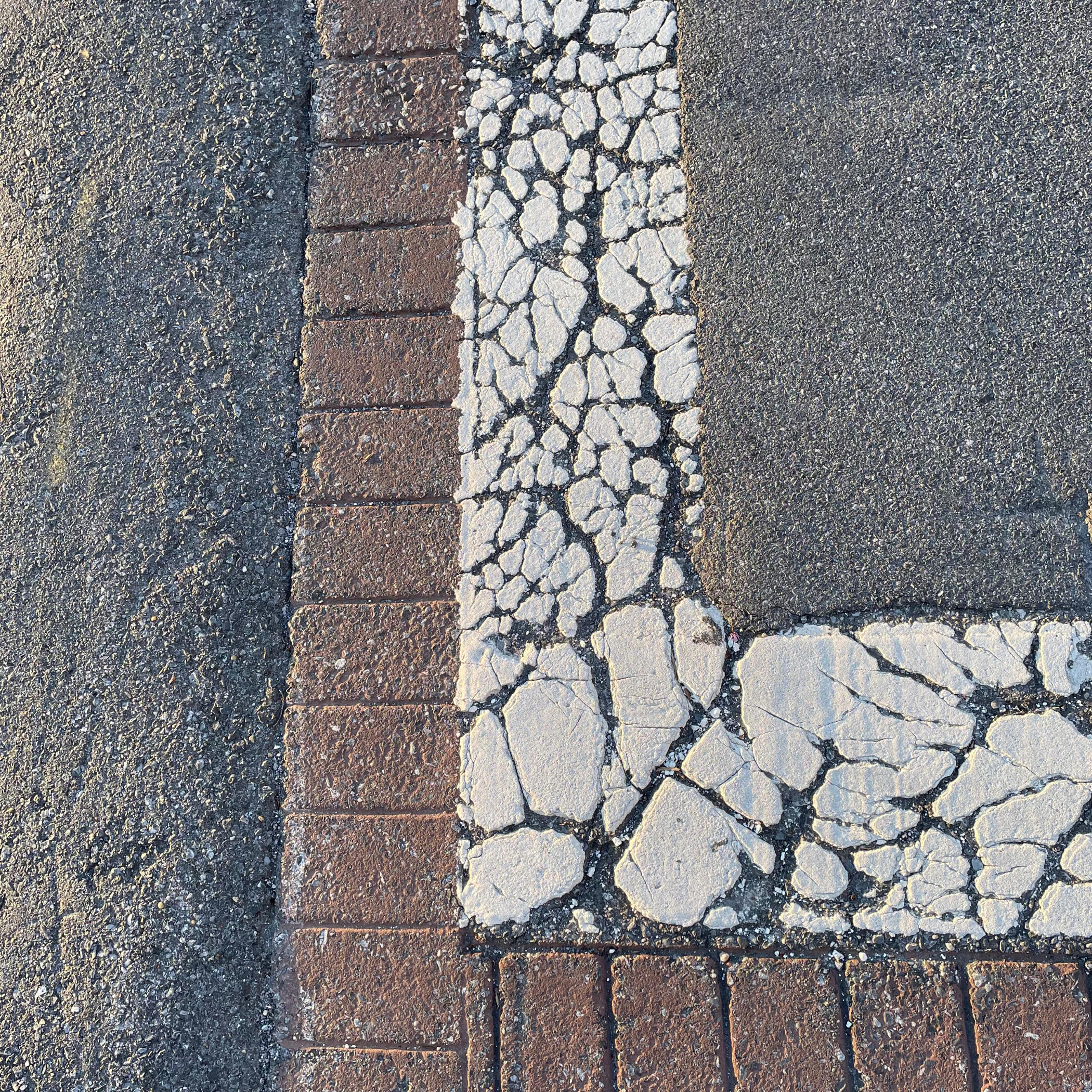 Cracked pavement with the word "NO" stenciled in yellow, next to a painted yellow lane dividing line.